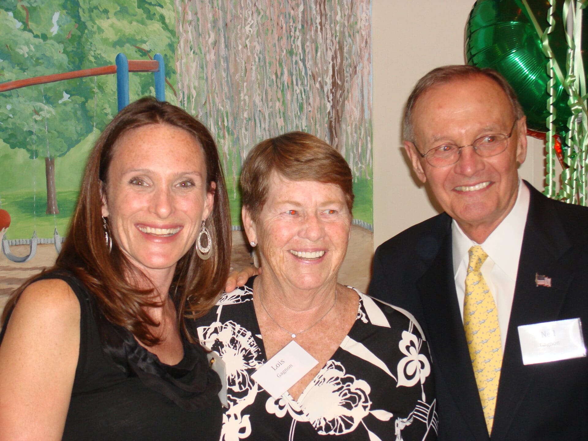 Two Women With a Man in Black Suit Infront of a Mural